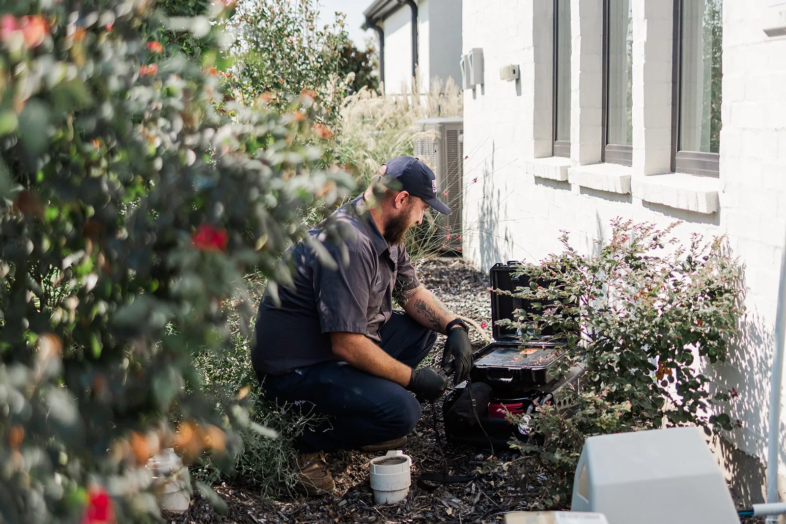 Plumber working drain equipment beside a home foundation