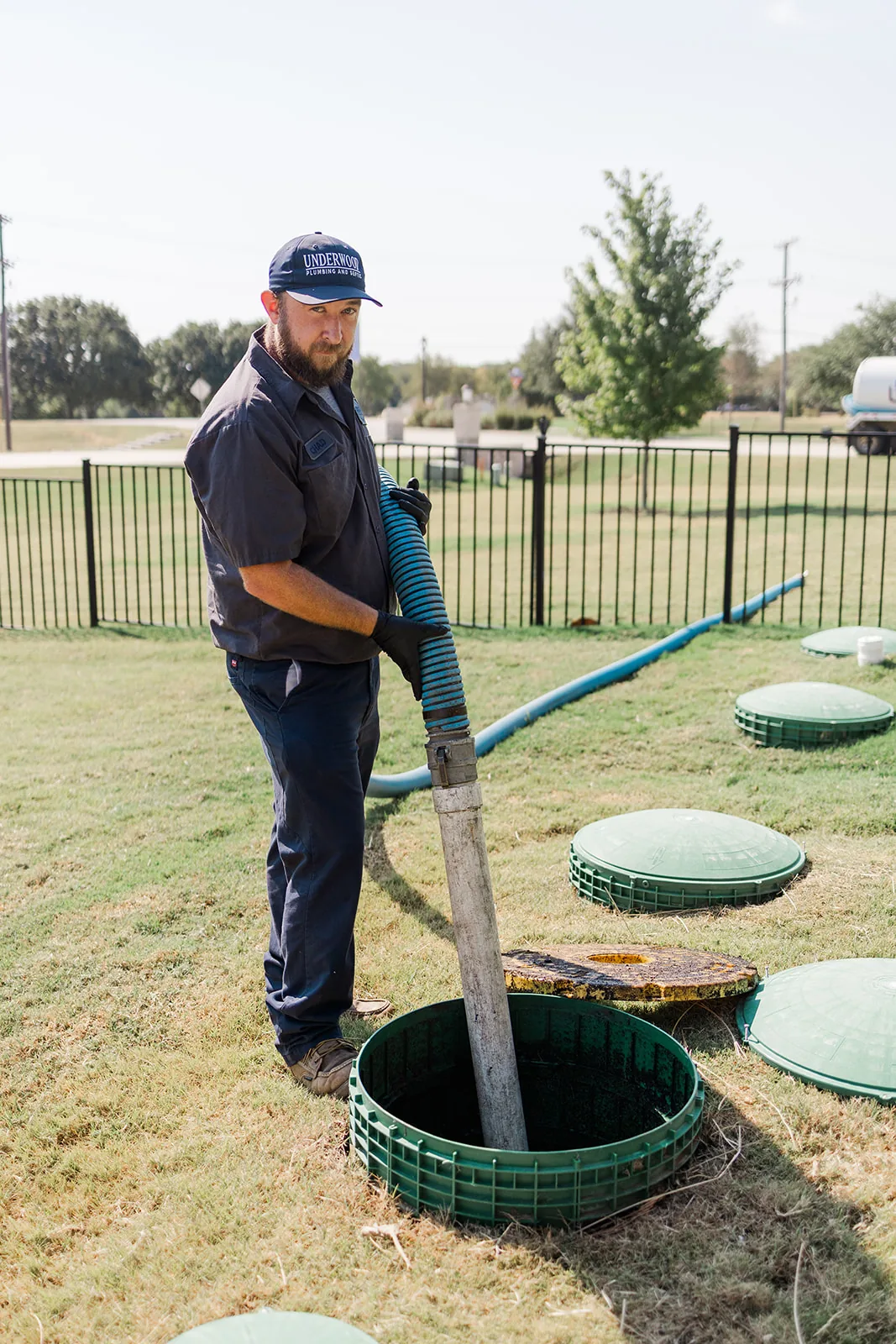 Septic technician guiding a pump hose into an open septic tank